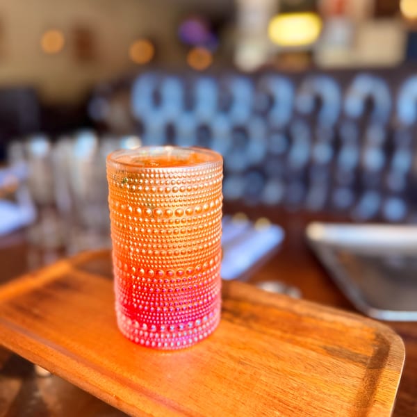 A vibrant orange and red textured glass candle holder sits on a wooden tray in a restaurant.