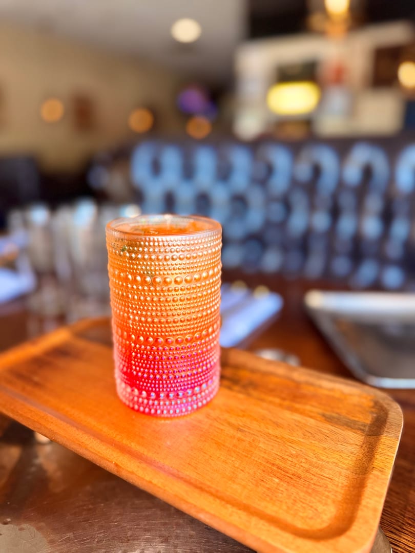 A vibrant orange and red textured glass candle holder sits on a wooden tray in a restaurant.