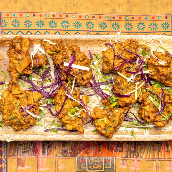 Crispy pakoras garnished with shredded red and white cabbage on a wooden platter.