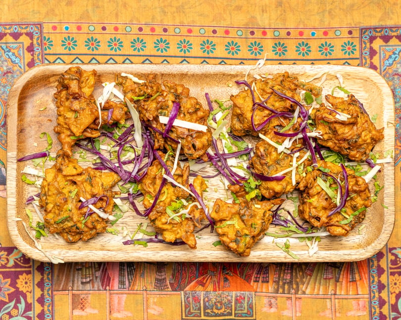 Crispy pakoras garnished with shredded red and white cabbage on a wooden platter.