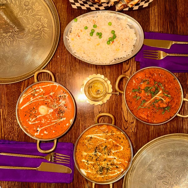 Overhead view of three Indian curries, rice, and naan bread on a wooden table.