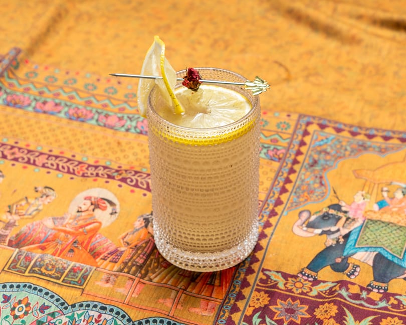 A refreshing lemon drink with a lemon slice and a dried rosebud garnish on a patterned yellow tablecloth.