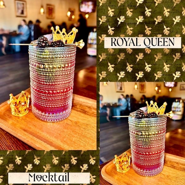 A vibrant mocktail with blackberries and a golden crown garnish, on a wooden tray in a restaurant.