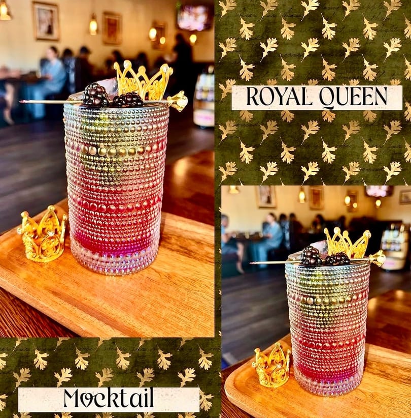 A vibrant mocktail with blackberries and a golden crown garnish, on a wooden tray in a restaurant.