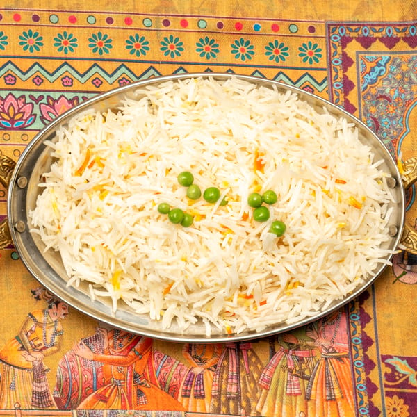 Basmati rice with green peas and saffron threads in a silver serving dish on a colorful patterned tablecloth.