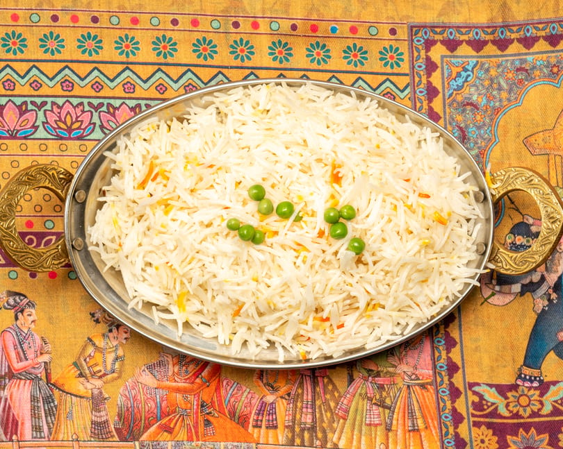 Basmati rice with green peas and saffron threads in a silver serving dish on a colorful patterned tablecloth.