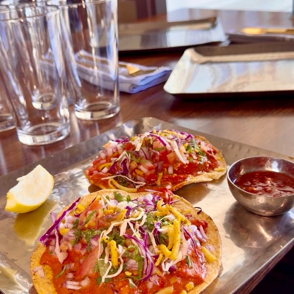 Two vibrant tostadas with red sauce, shredded cabbage, and cheese, served with a lemon wedge and salsa.