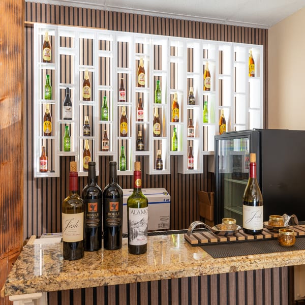 A bar area with a granite countertop, wine bottles, and a wall display of various beer bottles.