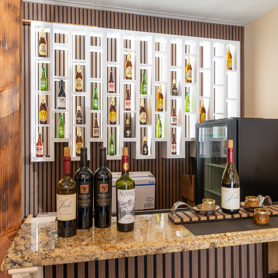 A bar area with a granite countertop, wine bottles, and a wall display of various beer bottles.