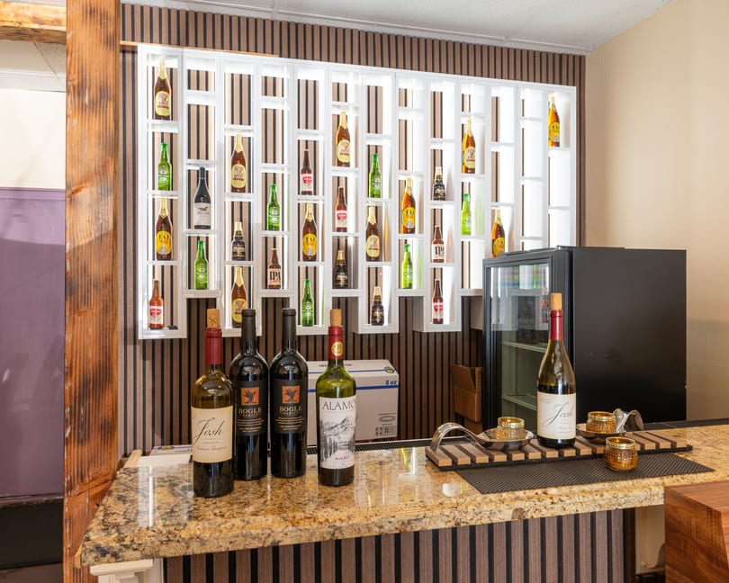 A bar area with a granite countertop, wine bottles, and a wall display of various beer bottles.