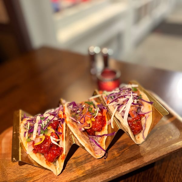 Three vibrant tacos with red meat and colorful slaw, served on a wooden tray.
