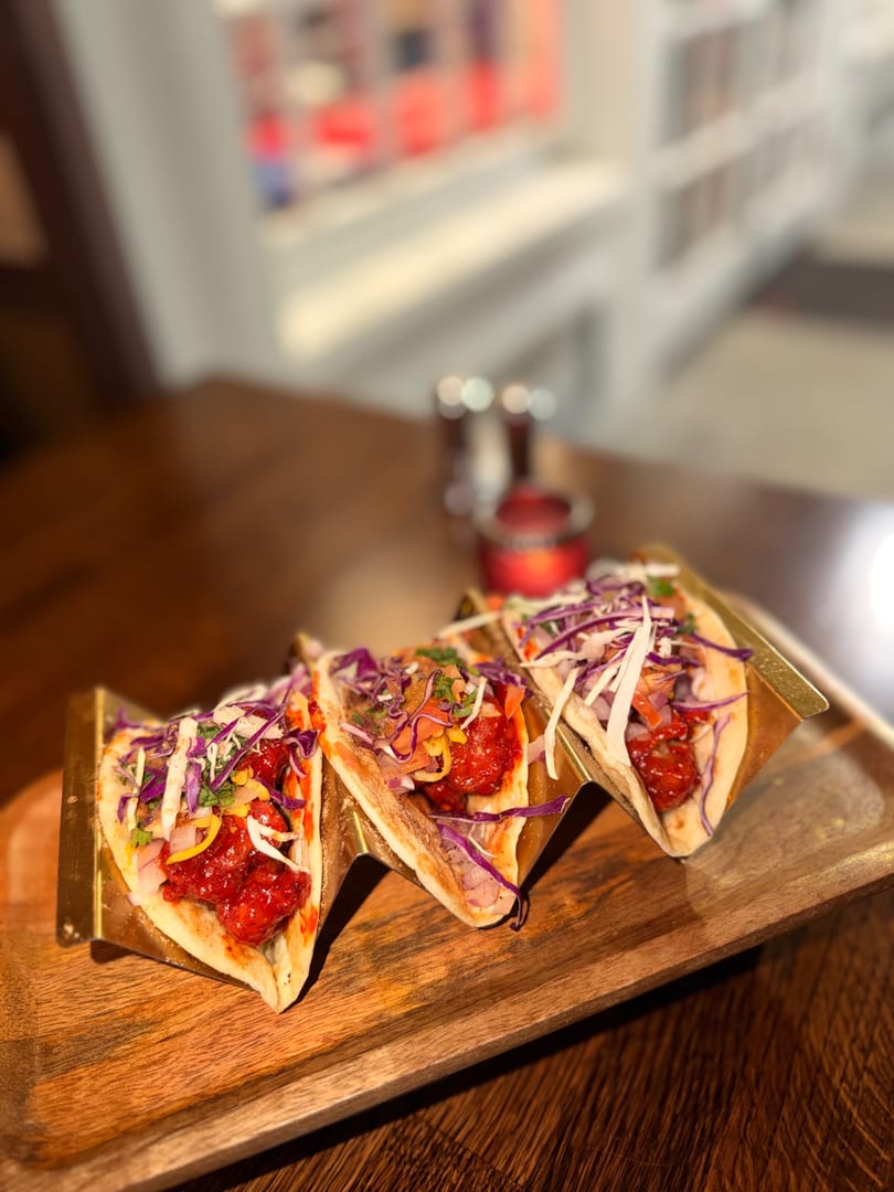 Three vibrant tacos with red meat and colorful slaw, served on a wooden tray.